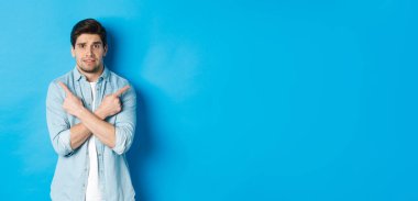 Tedirgin bir adamın portresi parmaklarını yana doğru gösteriyor, kararsız görünüyor ve seçimle ilgili yardım istiyor, sol ve sağ promosyon tekliflerini gösteriyor, mavi arka planda duruyor..