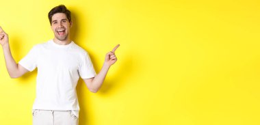 Mutlu stil sahibi adam iki farklı şey gösteriyor. Sol ve sağ tanıtımlarda parmaklarını yana doğru gösteriyor. Sarı arka planda duruyor..