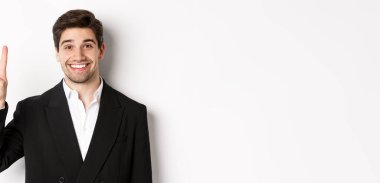 Siyah takım elbiseli yakışıklı iş adamının yakın çekimi, şaşkınlıkla gülümsüyor, dört numarayı gösteriyor, beyaz arka planda duruyor..