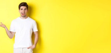 Kafası karışmış ve şok olmuş bir adam şikayet ediyor, bir elini kaldırıyor ve rahatsız görünüyor, sarı fotokopi alanının yanında duruyor..