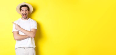 Turizm ve yaşam tarzı kavramı. Reklam veren mutlu genç erkek turist, solu işaret ediyor ve gülümsüyor heyecanlı, sarı arka plan.