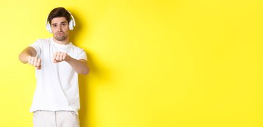 Kulaklıkla müzik dinleyen, dans eden, beyaz elbiseli, sarı stüdyo arka planında duran havalı adam..