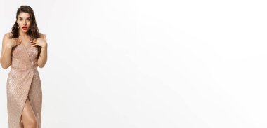 Noel partisi ve kutlama konsepti. Zarif elbiseli, uzun boylu, çekici bir kadın model. Şaşırmış ve kendini işaret ediyor. Beyaz arka planda duruyor..