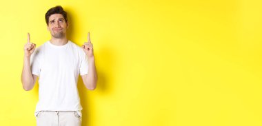 Şüpheci genç bir adam kötü bir şeyi işaret ediyor ve ona bakıyor, sarı arka planda duran bir teklifi yargılıyor..