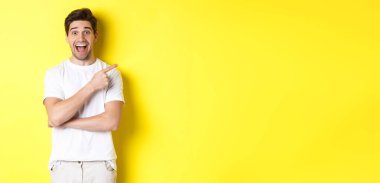 Heyecanlı gülümseyen bir adam resmi. Kara Cuma teklifleri sunuyor, parmağıyla işaret ediyor ve şaşırmış görünüyor. Sarı arka planda duruyor..