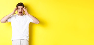 Şok olmuş, paniklemiş, el ele tutuşmuş, sarı arka planda duran sinirli bir adam..