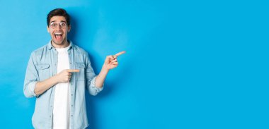 Mavi arka planda tanıtım teklifini gösteren, mavi arka planda duran, gözlüklü, tam fotokopi alanını gösteren şaşırtıcı bir adam..