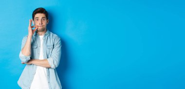 Ağzı sıkı yetişkin bir adam, söz ver sır tut, dudaklarını mühürle ve mavi arka planda dur..