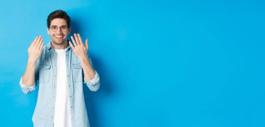 Manikür yapan, gülümseyen, tırnaklarıyla ilgilenen, mavi arka planda duran, gözlüklü yakışıklı genç adam..