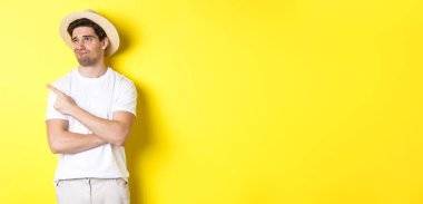 Turizm ve yaşam tarzı kavramı. Memnun olmayan erkek turist şikayetçi, sol üst köşedeki tanıtıma bakıyor ve işaret ediyor, hayal kırıklığıyla, sarı arka planda duruyor..