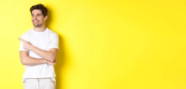 Beyaz elbiseli yakışıklı adam, sarı arka planda duran, sol pankarta bakıp işaret ediyor..