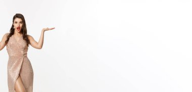 Noel partisi ve kutlama konsepti. Zarif elbiseli çekici esmer kadın manken, iki teklif sunuyor, el kaldırıyor ve fotokopi alanında bir şey tutuyor, beyaz arka plan..