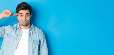 Aptal ya da deli gibi davranan, parmaklarını yuvarlayan ve mavi arka planda duran kameraya bakan adamı yakından çek..