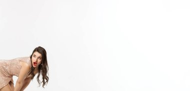 Noel partisi ve kutlama konsepti. Lüks elbiseli, uzun boylu, şehvetli esmer, eğil ve sola bak, şaşkın bir yüz, beyaz arka plan.