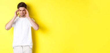 Başı ağrıyan, acı çeken, baş ağrısından şikayet eden, sarı arka planda duran sorunlu bir adam. Boşluğu kopyala