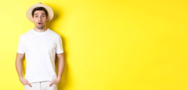 Seyahat ve turizm kavramı. Hasır şapkalı, şaşırmış, beyaz bir adam sarı arka planda duruyor..