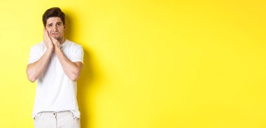 Üzgün adam diş ağrısından şikayetçi, kırlangıç yanağına dokunuyor ve üzgün görünüyor, sarı arka planda duruyor. Boşluğu kopyala