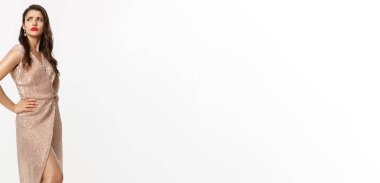 Noel partisi ve kutlama konsepti. Canı sıkkın, kaşlarını çatmış, yan yan yan bakan, şaşaalı bir elbise içinde beyaz arka planda duran kıskanç bir kadın..