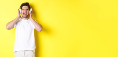 Mutlu adam yeni kulaklıkla müzik dinliyor, siyah cuma günü kulaklık alıyor, sarı arka planda dikiliyor..