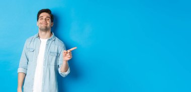 Kendine güveni tam olan yakışıklı adam küstah, parmağını fotokopi alanına doğrultuyor, reklamını yapıyor, mavi arka planda duruyor..