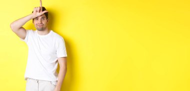 Alnında ezik işareti olan, üzgün ve kasvetli görünen, beyaz tişörtlü, sarı arka planda duran garip adam..