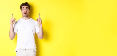 Etkilenmiş adam reklam teklifini kontrol ediyor, bakıyor ve işaret ediyor, sarı arka planda duruyor..