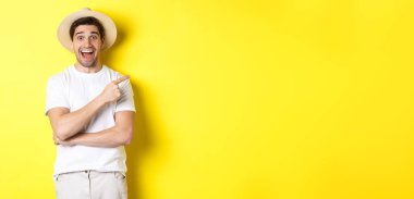 Hasır şapkalı mutlu erkek turist sağda, fotokopi alanında tanıtım teklifini gösteriyor, sarı arka planda. Boşluğu kopyala