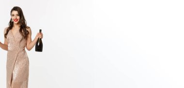 Noel partisi ve kutlama konsepti. Kırmızı dudaklı, lüks elbiseli, elinde bir bardak şampanya ve şişe olan zarif bir kadın..