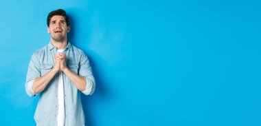 Çaresiz bir adam yardım için yalvarıyor, Tanrı 'ya yalvarıyor, el ele tutuşup dua ediyor, mavi arka plana karşı duruyor..