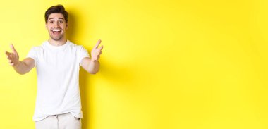 Heyecanlı yakışıklı adam elini uzatıyor, sarılıyor, hediyesini alıyor, sarı arka planda duruyor..