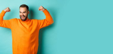 Genç ve güçlü görünümlü, kendinden emin, kaslı, kaslı, kendine güvenen, açık mavi arka planda duran genç ve güçlü bir adam..