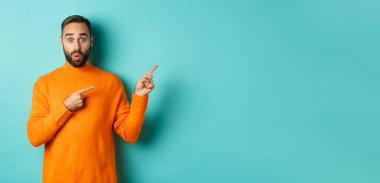 Reklam veren, pankartı işaret eden, turkuaz arka planda duran harika bir adam..