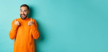 Sakallı heyecanlı genç adam, onaylama, övme ya da tavsiye, açık mavi arka planda duruyor..