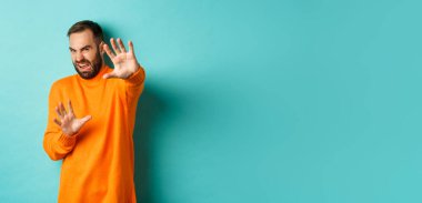 Tiksinmiş adam korunmak için el pençe divan durur, merhamet için yalvarır, nefretle dolu bir şeye bakar, açık mavi arka planda durur..