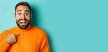 Mutlu genç adama yakın çekim. Kendini sürpriz ve heyecanla gösteriyor. Açık mavi arka planda duruyor..