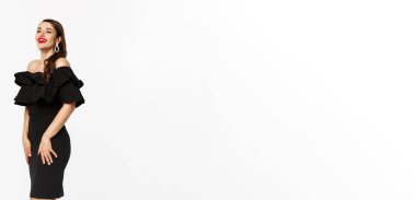 Lüks elbiseli, kırmızı dudaklı ve takılı güzel bir kadının dikey görüntüsü. Beyaz arka planda duran Noel hediyeleriyle birlikte..