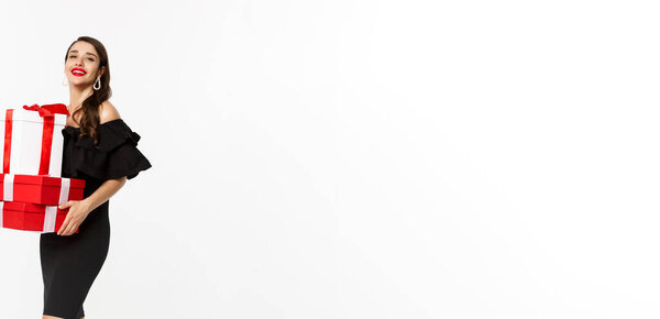 Полная длина элегантной женщины в черном платье, красные губы, проведение рождественские подарки и улыбаясь приятно, получать подарки, стоя на белом фоне.