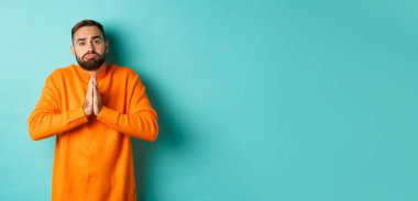 Somurtkan adam yardım dileniyor, iyilik istiyor, el ele tutuşup dua ediyor ve somurtuyor, turkuaz arka planda duruyor..