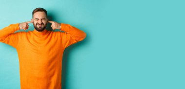 Hoşnut olmayan adam kulaklarını kapattı ve suratını buruşturan, gürültücü komşular, gürültüden rahatsız, açık mavi arka plan.