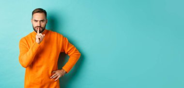 Kızgın sakallı adam sessiz olun diyor, susun ve hoşnutsuz olun, çenenizi kapayın jestlerinizi, turkuaz arka planda durun.