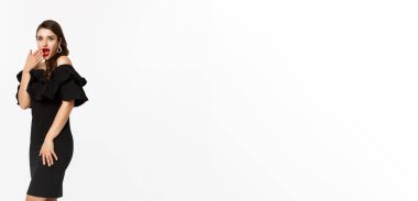 Zarif elbiseli ve kırmızı dudaklı bir kadın, şaşırmış görünüyor, Noel tatilinde hediyeler alıyor, beyaz arka planda hediyeler sunuyor..