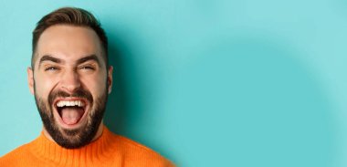 Sakallı, mutlu ve kaygısız bir adamın portakal rengi kazak giymiş kameraya bakıp gülüşü..