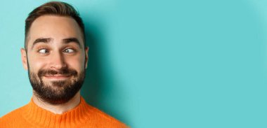 Kafkasyalı komik bir adamın suratını, gözlerini kısarak ve gülümseyerek, açık mavi arka planın üzerinde durduğu bir vesikalık..