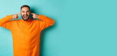 Hoşnut olmayan adam kulaklarını kapattı ve suratını buruşturan, gürültülü komşular, gürültüden rahatsız olmuş, kızgın ve sıkıntılı, açık mavi arka plan.