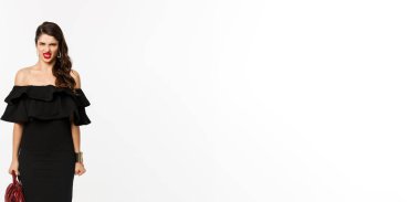 Güzellik ve moda konsepti. Siyah parti elbisesi ve yüksek topuklu ayakkabı giymiş kızgın bir kadın. Kameraya karşı küçümseyen ve suratını buruşturan biri..