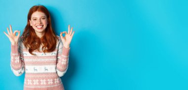 Süveter giyen güzel bir kızıl kız. Gülümsüyor. Memnun, onaylıyor ve övüyor..