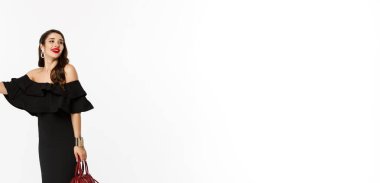 Güzellik ve moda konsepti. Siyah elbiseli, topuklu ayakkabılı, taksiyi durdurmak için elini kaldıran çekici bir kadın. Bir araca ihtiyacı var. Beyaz arka planda duruyor..