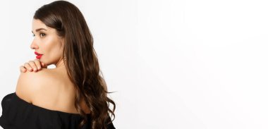 Moda ve güzellik konsepti. Zarif bir kadın omzuna yaslanıyor ve şehvetli delici gözlerle yan yana bakıyor, makyaj yapıyor ve kırmızı ruj sürüyor, beyaz arka planda duruyor..