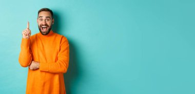 Yakışıklı beyaz adamın bir fikri var, parmağını kaldırıyor ve planını söylüyor, turkuaz arka plana karşı heyecanlı duruyor..