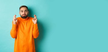 Umut dolu üzgün adam bir dilek diliyor, şans diliyor ve somurtuyor, turkuaz arka planda duruyor..